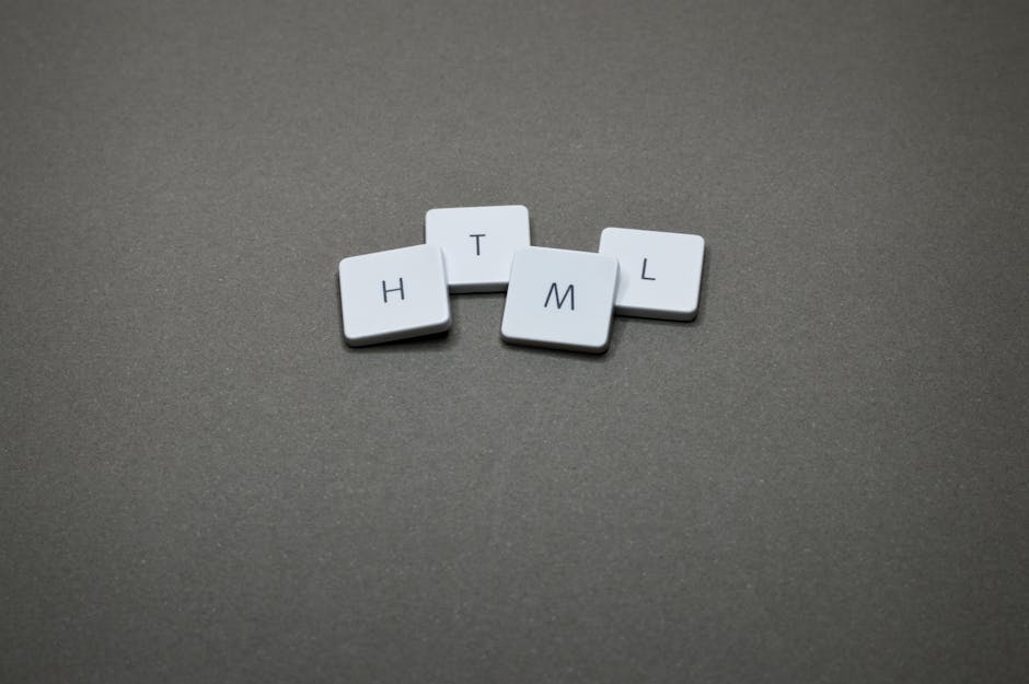 Four small white tiles with black letters arranged on a grey surface spell out the word 'HTML', with the tiles positioned in a slightly scattered manner. The tiles are made of plastic or similar mater